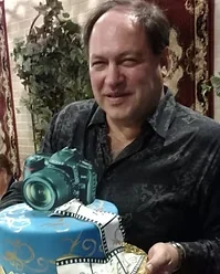 Leon Treskunov smiling beside a celebration cake decorated with a camera at the store