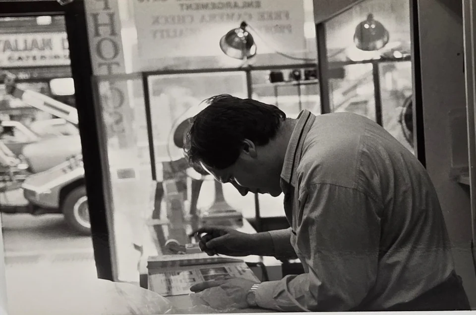 Leon Treskunov leaning over his repair work by a Manhattan shop window in 1989