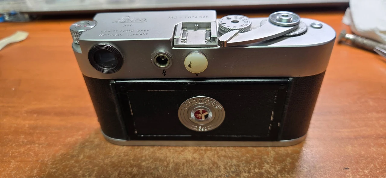 Leica M2 rear after repair, with textured black replacement skin across the rear panel and sides, and the silver top cover and film reminder dial in place.